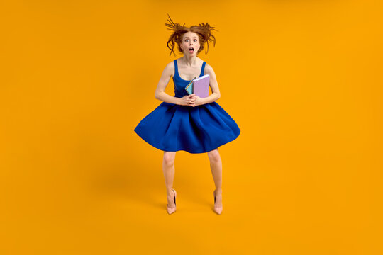 Funny amazed teacher woman in blue dress holding books in hands, in shock by pupils, wearing high-heels, rde hair is flying. 1 september, education, school concept