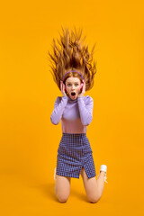 Excited Funny Female With Flying Long Red Hair Is In Shock By Listening Music So Loud, Look At Camera With Surprised Facial Expression, Opening Mouth By Shock, Isolated On Bright Yellow Background