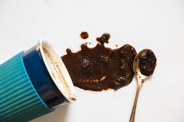 a cup with overturned coffee on a white background and a teaspoon lies next to it, spilled coffee...