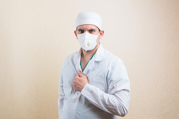 Young doctor in white suit and protective breathing mask with his hand on his chest on the yellow background isolated.