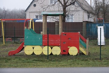 playground with a colored wooden steam locomotive in green grass outside behind a metal mesh fence