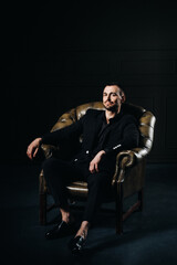 Fototapeta na wymiar portrait of an elegant young European man in a suit sitting on a chair in a dark interior