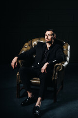 Fototapeta na wymiar portrait of an elegant young European man in a suit sitting on a chair in a dark interior