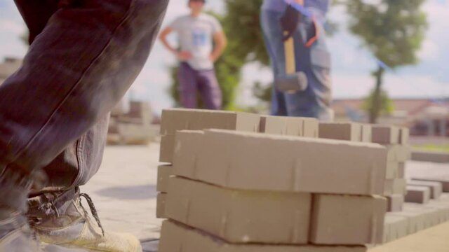 A worker at the back, dressed in work pants, pulls a thread or rope to align the laying of paving slabs. Construction, laying paving slabs by a team on a sunny day.