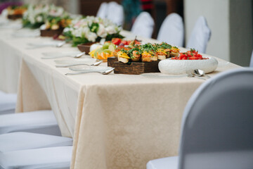 Beautifully laid dining table outdoors, abundant in the food. Dishes layed in a straight line on a thick wooden boards and plates.