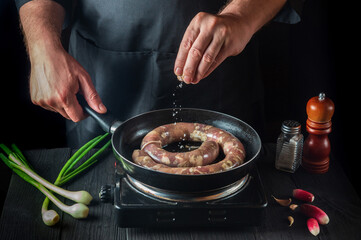 The chef adds salt to pan with raw meat sausage. Preparation for cooking sausages in the kitchen of a restaurant or cafe on table with vegetables and spices