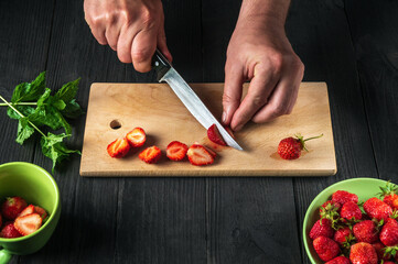 Close-up chef hands cut fresh strawberries on cutting board of restaurant kitchen for making soft drink with mint. Cooking diet desserts