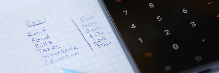 Monthly expenses are written on piece of paper with calculator
