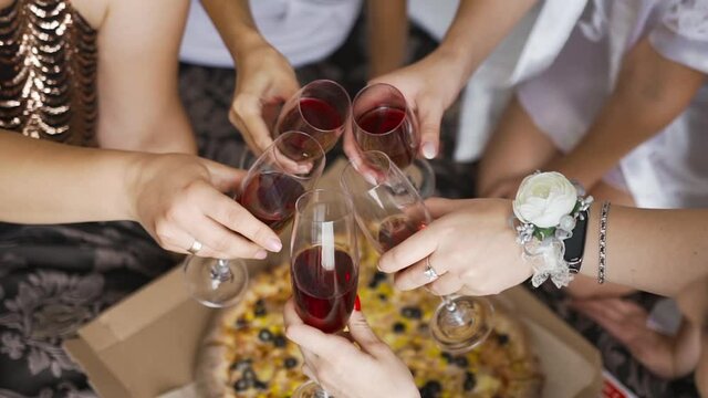 Company of girls having fun and rumble glasses of alcohol on background of round baked pizza. Red wine or champagne. Delicious and fragrant Italian pizza with dough and various ingredients