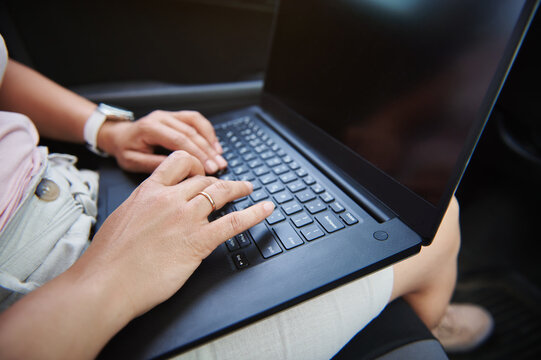 Close-up image of business woman hands typing a text message on laptop while sitting in driver seat in the car