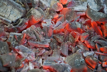 Embers of red and black color. Many burning out coals lie nearby. Some coals have already formed white ash. Some of the coals glow red.