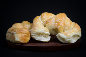 2 croissants with a syrup bath, on a wooden plate. Black background