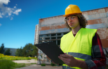 Male contractor in hard hat inspects abandoned buildings.