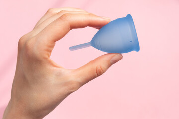 Elegant lady hand shows contemporary light blue silicone menstrual cup on colorful pink background...