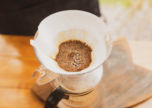 Barista making coffee pouring hot water on paper filter on top of glass coffee jar. Brazilian organic artisanal bakery small business concept.