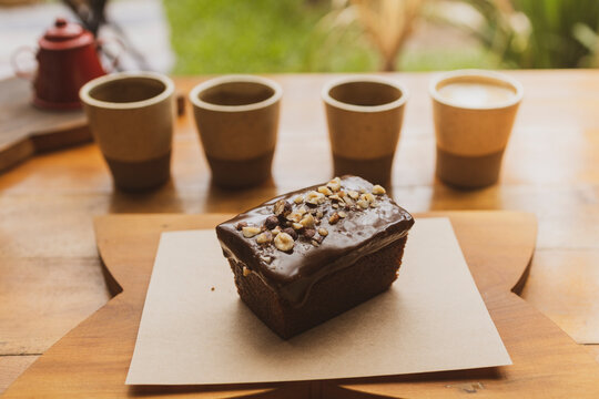 Natural organic chocolate brownie cake with nuts and chocolate cream on top., coffee cups out of focus on the background. Brazilian organic artisanal bakery mall business concept.