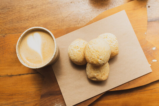 Brazilian organic artisanal bakery serving breakfast with a coffee mug and delicious cheese bread "p&atilde;o de queijo" sitting on top of a natural color wooden table.