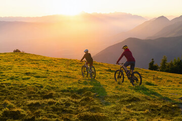 Mother and daughter cycling on mountain bikes at a sunset in mountains.