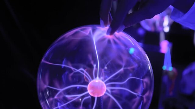 Woman hand touching plasma ball with many energy rays inside in dark room of interactive museum or exhibition - close up view. Electricity, education, science, futuristic and physics concept