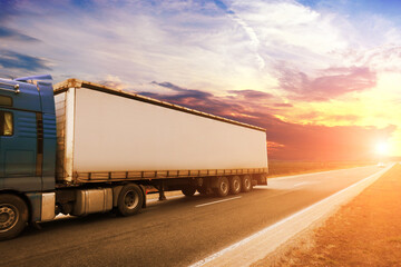 A big truck with a trailer on a road with other cars against a sky with a sunset
