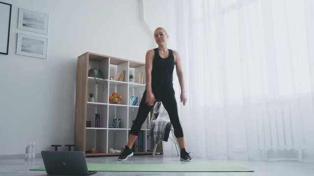 Aerobic fitness. Sportive woman. Online training. Home gym. Keep healthy body. Happy lady in black sportswear enjoying doing step workout looking laptop light room interior.