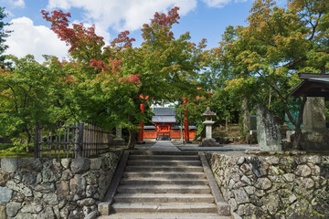 Entrance with torri gate sourrounded by maple trees at the temple Hachiman Daibosatsu in Arashiyama, Kyoto, Japan