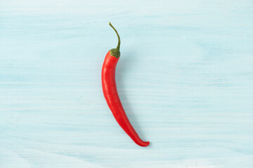 Single red chili pepper on a blue wood background