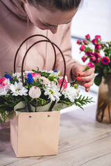 Female picking up bouquet of different flowers in paper gift bag with handles. Vertical