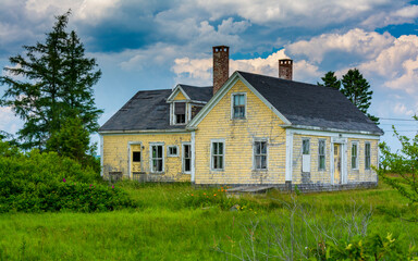 Obraz premium Old and abandoned house in rural Maine with dramatic clouds overhead on summer's day.