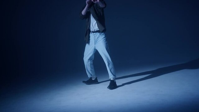 Young blonde guy dancing modern choreography in dark studio background. Talented choreographer man showing the new hip hop movements. Shooting a dance video clip. Hip hop school for teenagers. 
