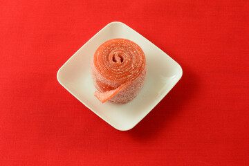 Sour strawberry fruit roll up candy in white candy dish on red background