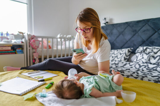 Caucasian woman young mother taking photo of her newborn child baby daughter while bottle feeding on the bed at home using mobile phone real people modern motherhood concept