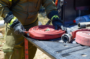 Person in fireman uniform packing a red water hose into a spiral