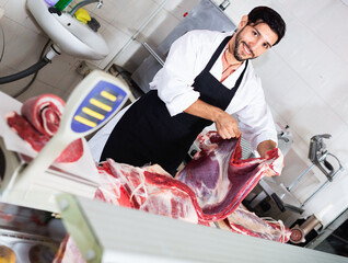 Smilling positive butcher is offering meat to clients in market.