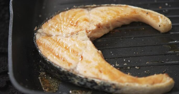 Juicy Salmon fish steak on hot black pan, Seafood on the grill- close up detail.
