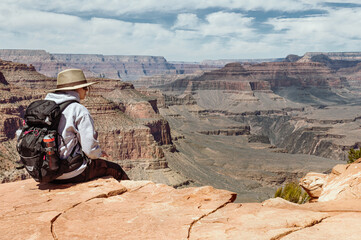 a teenaged girl hiker with a backpack and a bottle sitting on a cliff over the view of Grand Canyon