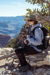 Vertical photo of a teeneger girl sitting on the rock having the rest over the view of Grand Canyon, Arizona, USA