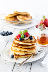 Close up of a stack of buttermilk pancakes, topped with fresh berries and banana slices and served with maple syrup.