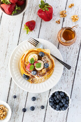 Top down vertical view of a stack of buttermilk pancakes served with fresh berries and syrup, ready for eating.