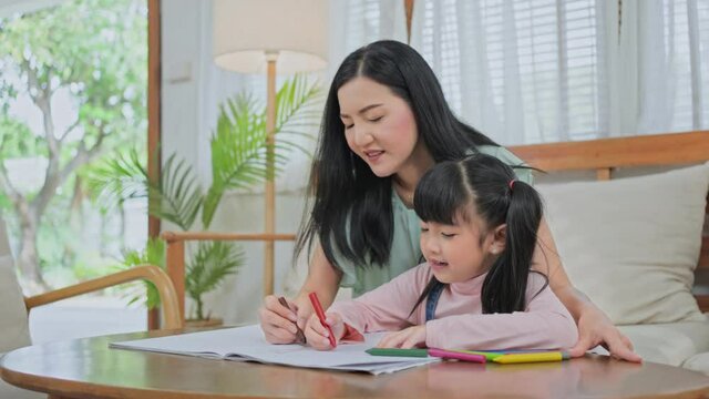 Asian little girl painting picture with mother in the living room.	