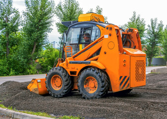 Orange color Skid steer loader with a many purpose bucket is using in landscaping.