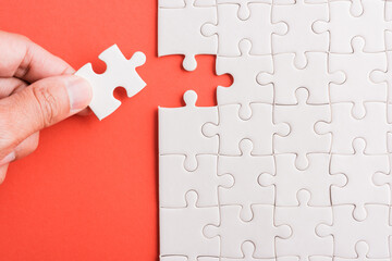 Top view flat lay of hand-holding last piece white paper jigsaw puzzle game last pieces put to...