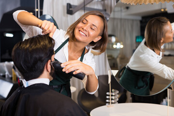 portrait of woman hairdresser shaving hair of smiling man in salon