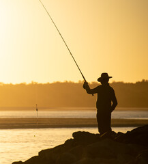 Close Up Silhouette of Fisherman on Rocks Against Sky at Sunset in Noosa, Queensland, Australia