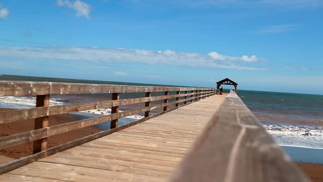 Close-Up Slow Motion Shot Of Pier At Beach By Coastline On Sunny Day Against Cloudy Sky - Kauai, Hawaii