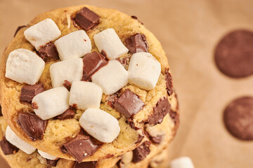 PRIMER PLANO DE GALLETAS UNA SOBRE OTRA CON CHIP DE CHOCOLATE Y MASMELLOS EN UNA TABLA CON PAPEL CAFE