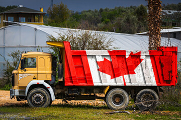 Dump truck with the image of the national flag of Canada is parked against the background of the countryside. The concept of export-import, transportation, national delivery of goods
