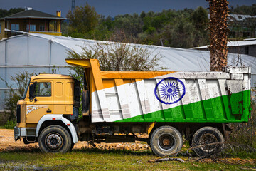 Dump truck with the image of the national flag of India is parked against the background of the countryside. The concept of export-import, transportation, national delivery of goods © Виталий Сова