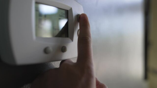 This close up video shows an anonymous hand pressing the buttons to change temperatures of an indoor thermostat.