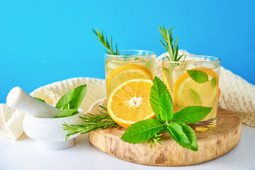 Summer refreshment drink. Glass of water with orange, mint and rosemary on blue background....